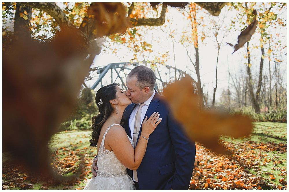 Couple kissing under autumn leaves near a bridge.
