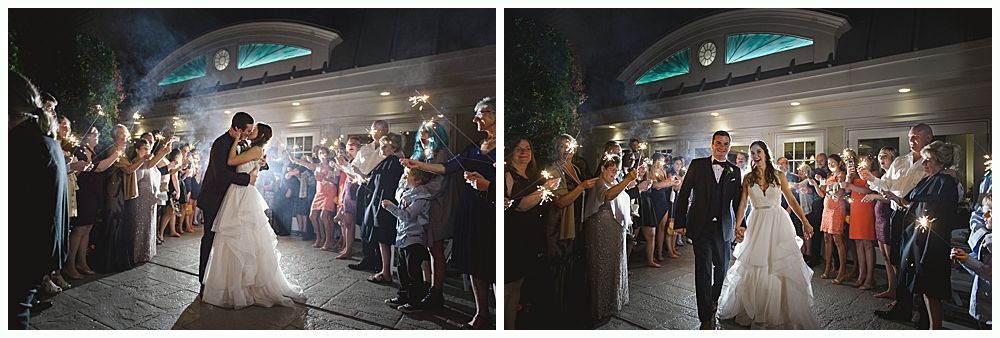 Couple kissing and walking through guests holding sparklers, illuminated at night. Wedding celebration.