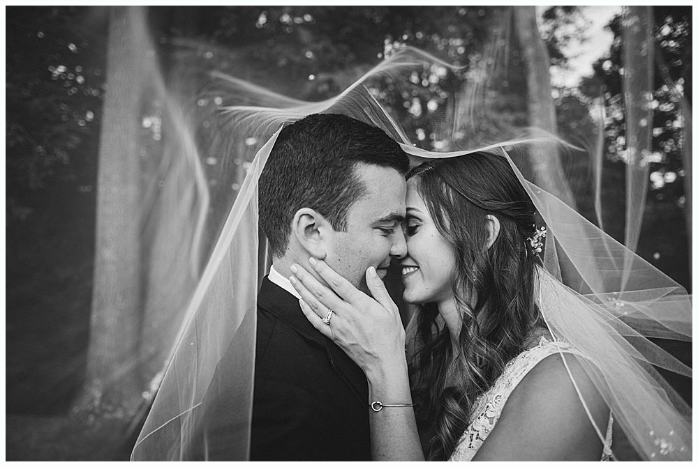 Newlyweds share an intimate moment, veiled in sheer fabric, smiling and touching faces.
