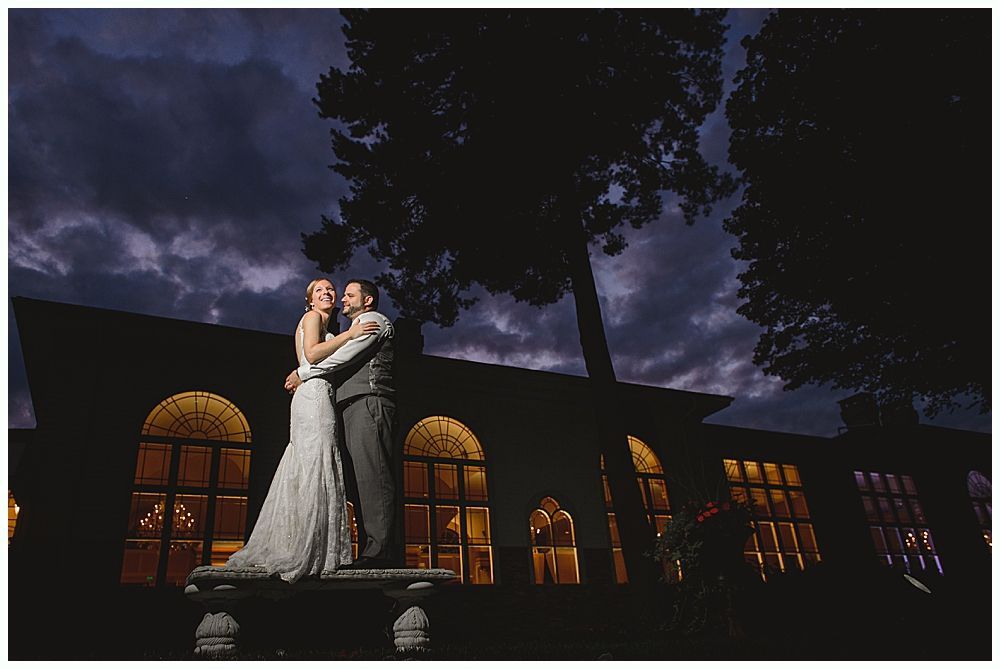 Couple embracing on bench, illuminated by building windows at dusk.