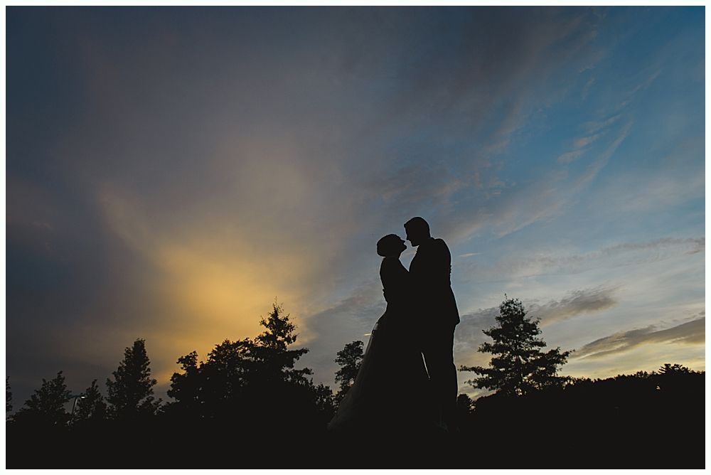 Silhouetted couple embracing against a sunset sky. Trees line the bottom.