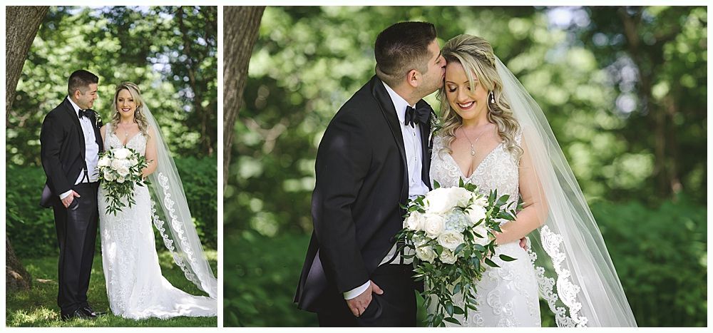 Bride and groom pose outdoors. The man kisses the woman's forehead. They are dressed for a wedding.