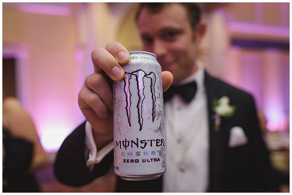 Man in formal attire holds up a Monster Zero Ultra energy drink can.