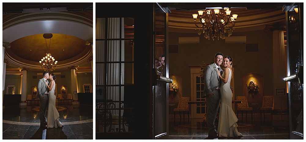 Couple embraces in a dimly lit ballroom. A chandelier hangs above them.