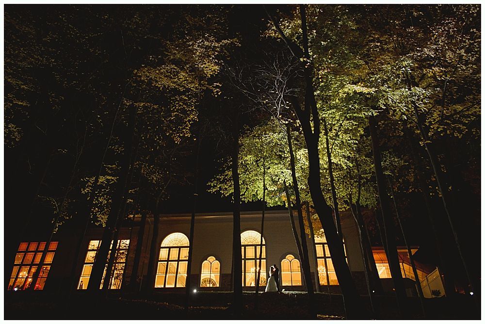 Building lit up at night, with trees in the foreground. Soft light shines from arched windows.