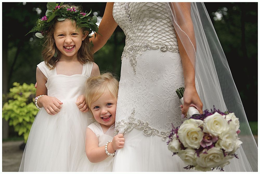 Bride with two flower girls, one with a floral crown, all smiling.