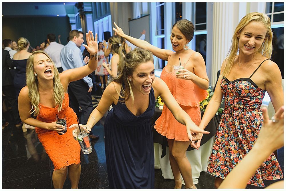 People dancing and laughing at a party, with drinks, in a brightly lit room.