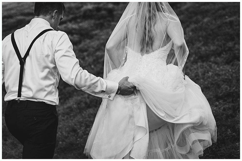 Groom helping bride with her wedding dress train outdoors. Black and white photo.
