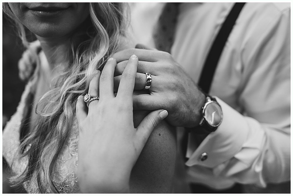Hands of a couple, one on the shoulder, wearing rings, watch and formal shirt.