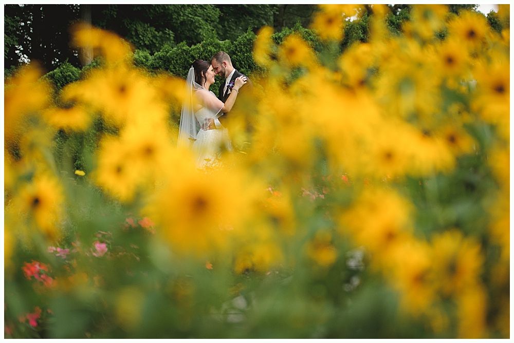 Wedding party: Bride in white dress surrounded by bridesmaids in blue, groomsmen in black, outdoors.