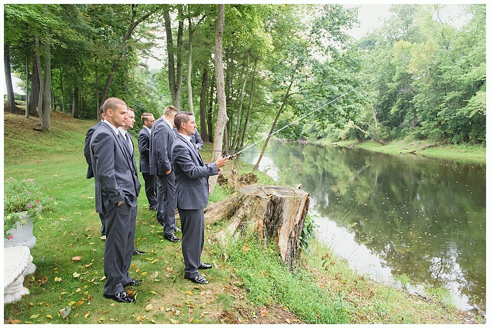 Men in suits fishing by a river, surrounded by trees.