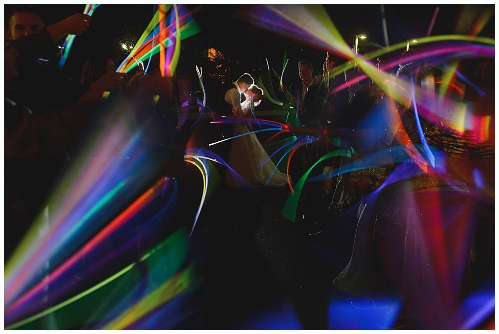 People at a party waving colorful glow sticks in a darkened room, streaks of light visible.
