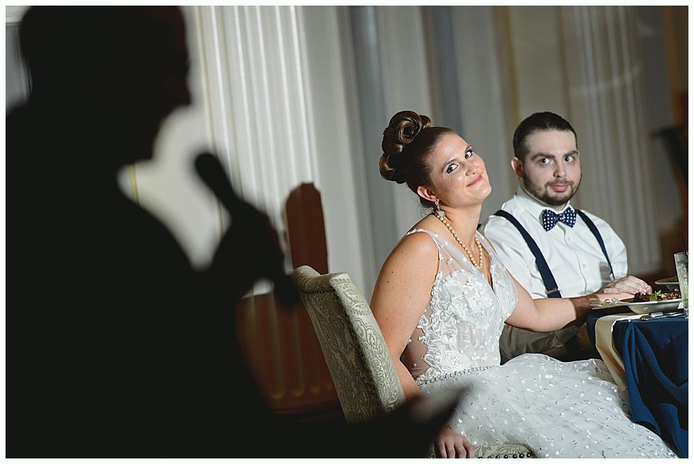 Bride and groom at a wedding reception; speaker's shadow in the foreground. They are smiling, sitting at a table.