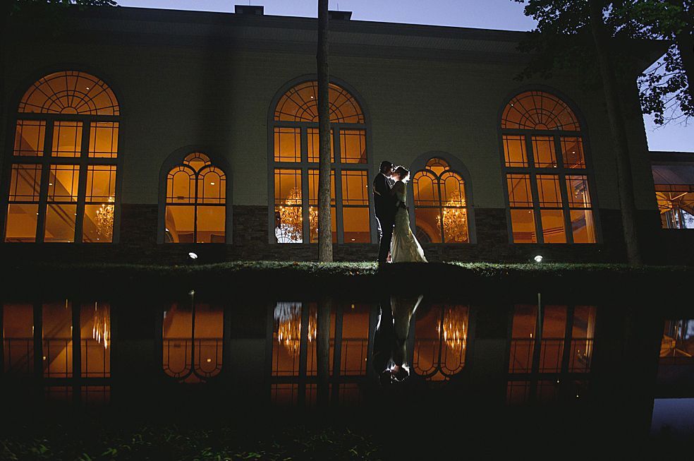 Couple dancing in front of a building with glowing windows; reflection in water below.