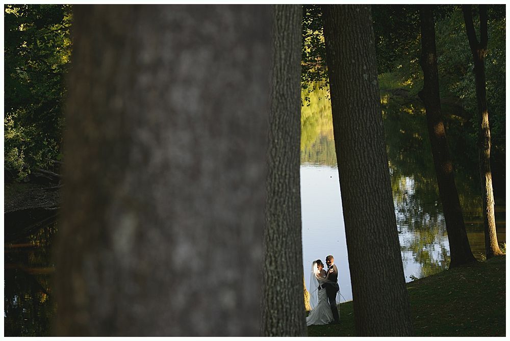 Wedding party smiles for photo outdoors. Bride, groom, bridesmaids, groomsmen, wearing black attire, holding bouquets.