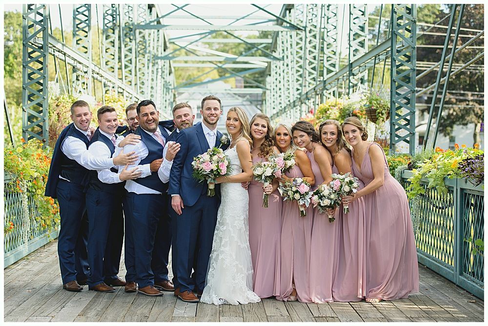 Wedding party on a bridge: bride and groom, bridesmaids in pink, groomsmen in navy.
