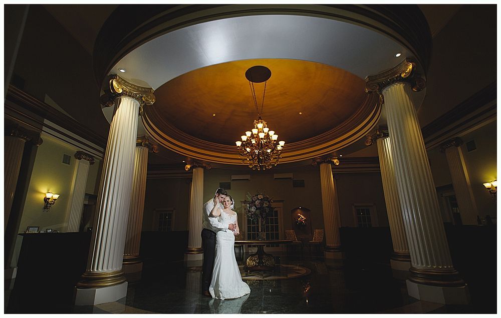 Couple dancing, silhouetted. Bride in wedding dress, groom in suit, under chandeliers.