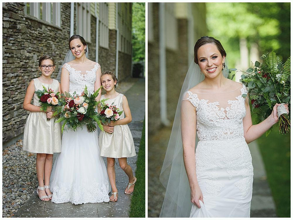 Bride with two flower girls, holding bouquets, by a stone building.