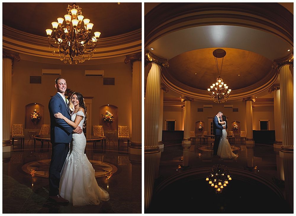 Wedding couple embracing in a grand hall with chandeliers, ornate ceiling, and reflective floor.