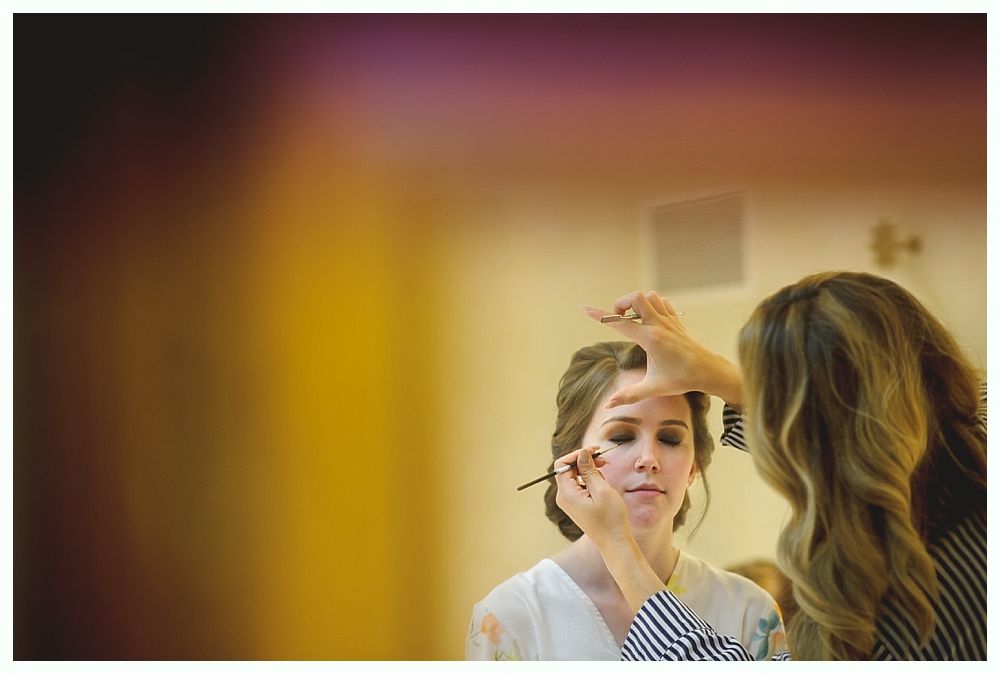 Woman has makeup applied by another person in a room, soft light.