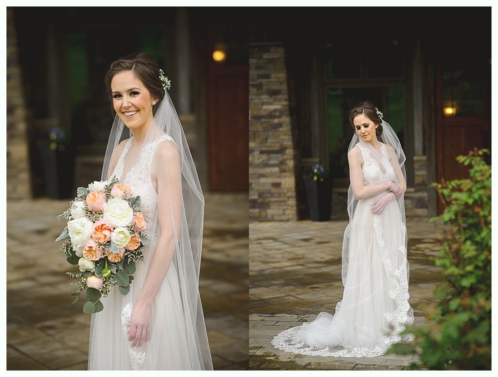 Bride in a white lace wedding dress, veil, and bouquet, smiles outdoors.