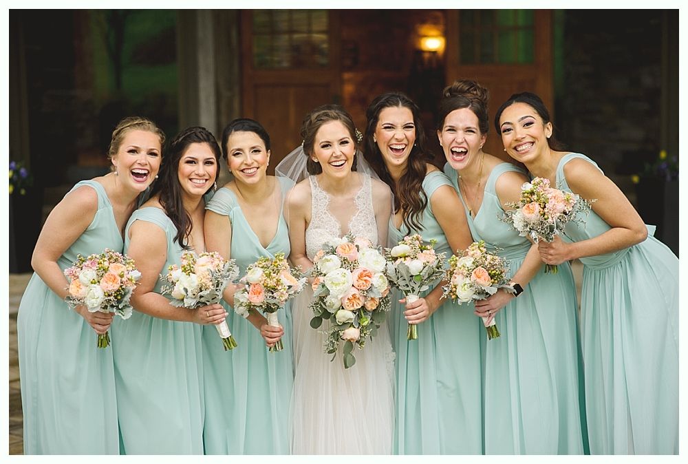 Bride and bridesmaids in mint-colored dresses, holding bouquets, laughing in front of a building.