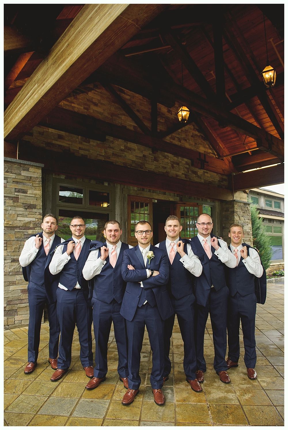 Group of men in blue suits, pink ties posing under a covered entrance.