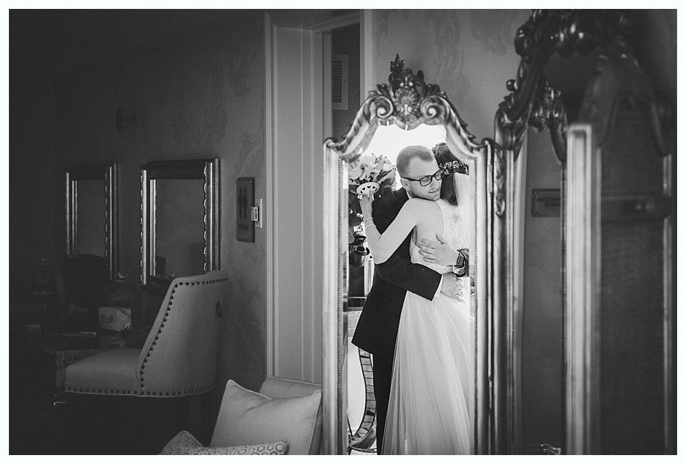 Bride and groom embrace in front of a ornate mirror.