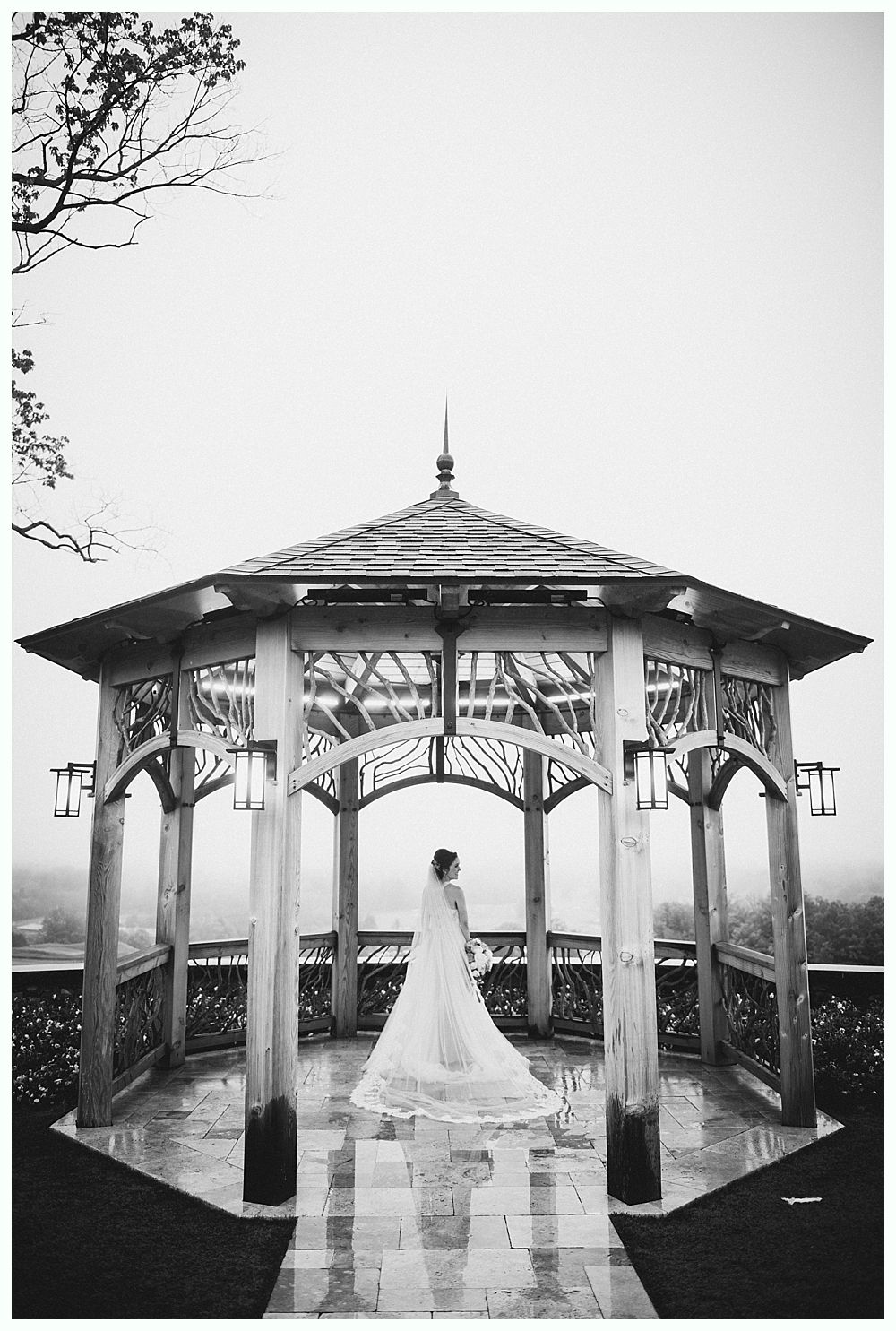 Bride in a wedding dress stands in a gazebo overlooking a foggy landscape.