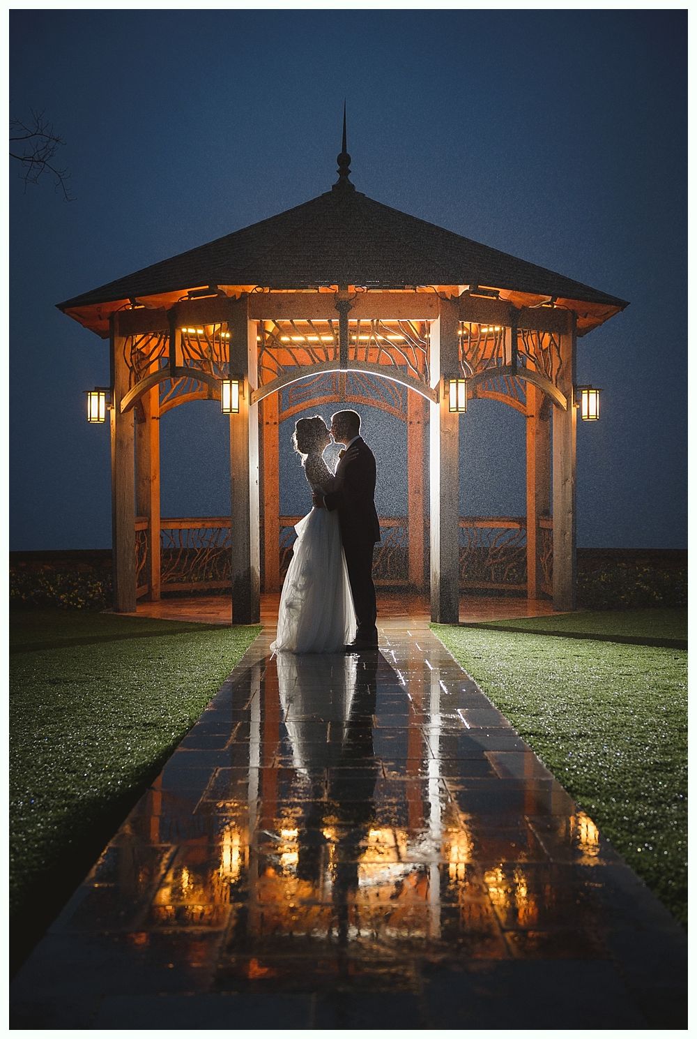 Wedding couple in gazebo, night. Lights reflect in wet walkway.