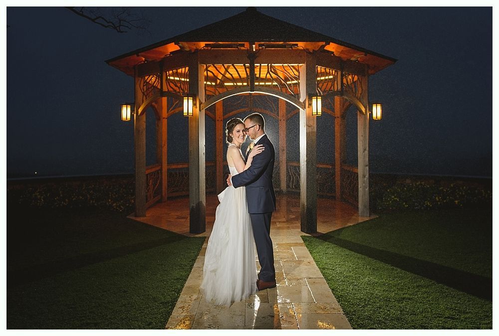Couple embracing under a lit gazebo at night, posing for a wedding photo.