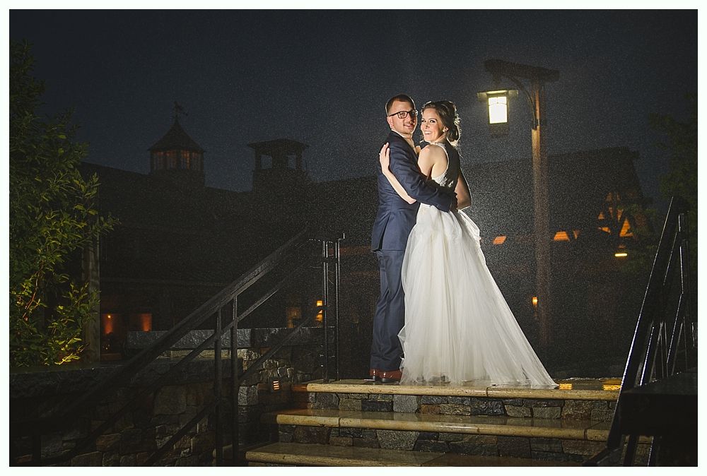 Couple embracing on stone steps at night in front of a barn with lights.