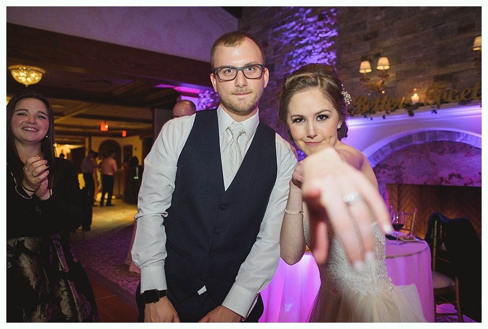 Bride shows off ring, groom smiles, party with archway, purple uplighting.
