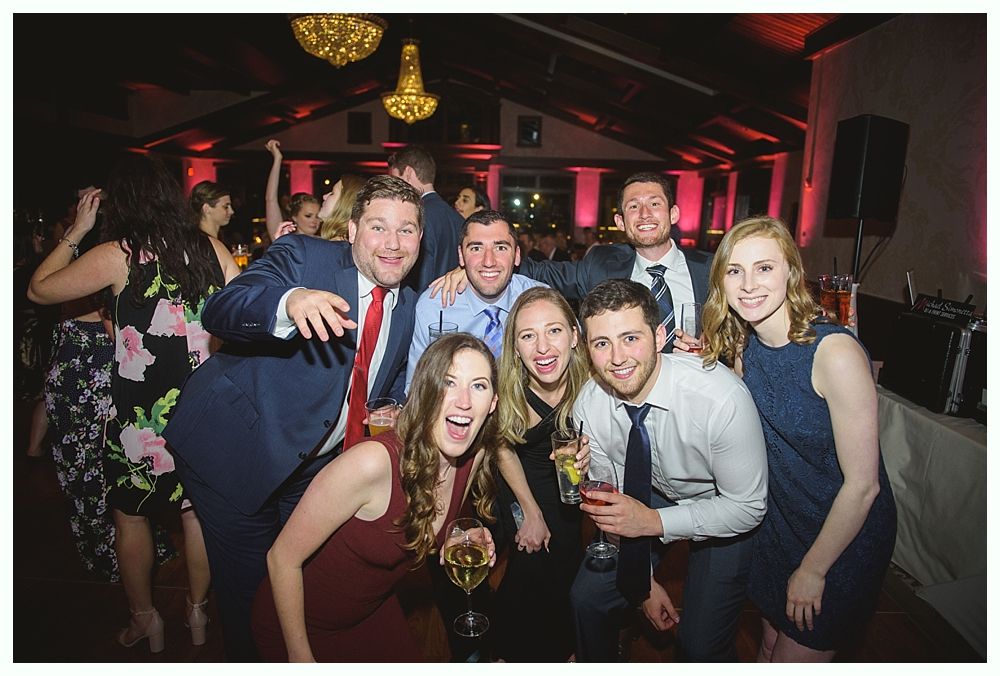 Group of people smiling, partying at a celebration with red lighting and a chandelier.