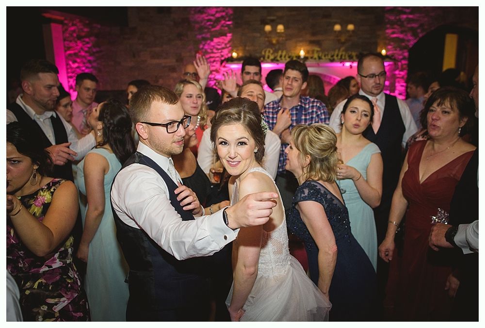 Wedding reception: bride and groom dancing with guests. Pink-lit room.