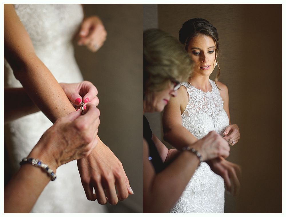 Bride in white lace dress, having bracelet fastened by another person. Well lit.