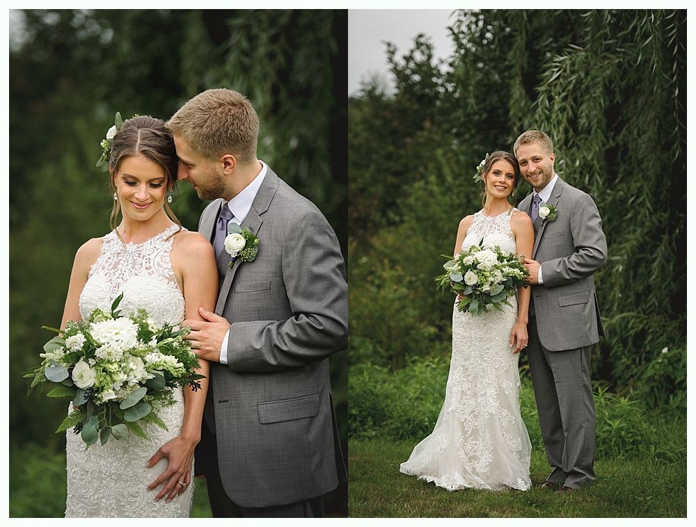 Bride and groom pose outdoors. She wears a lace wedding dress, he wears a gray suit.