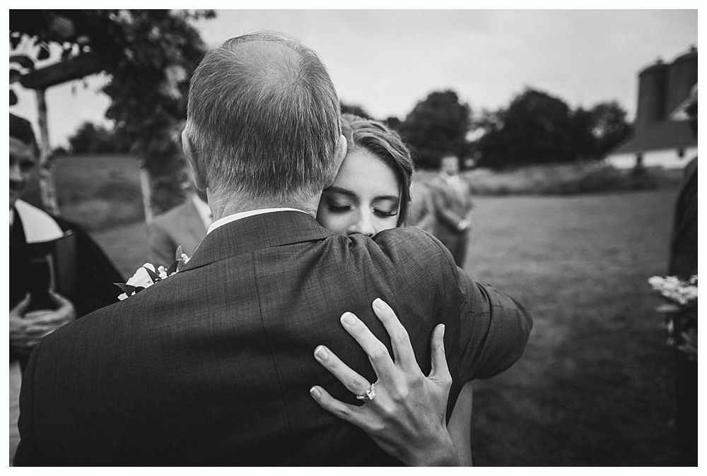 Bride embraces person in suit, close-up of arms and hands. Wedding ceremony outdoors. Black and white.