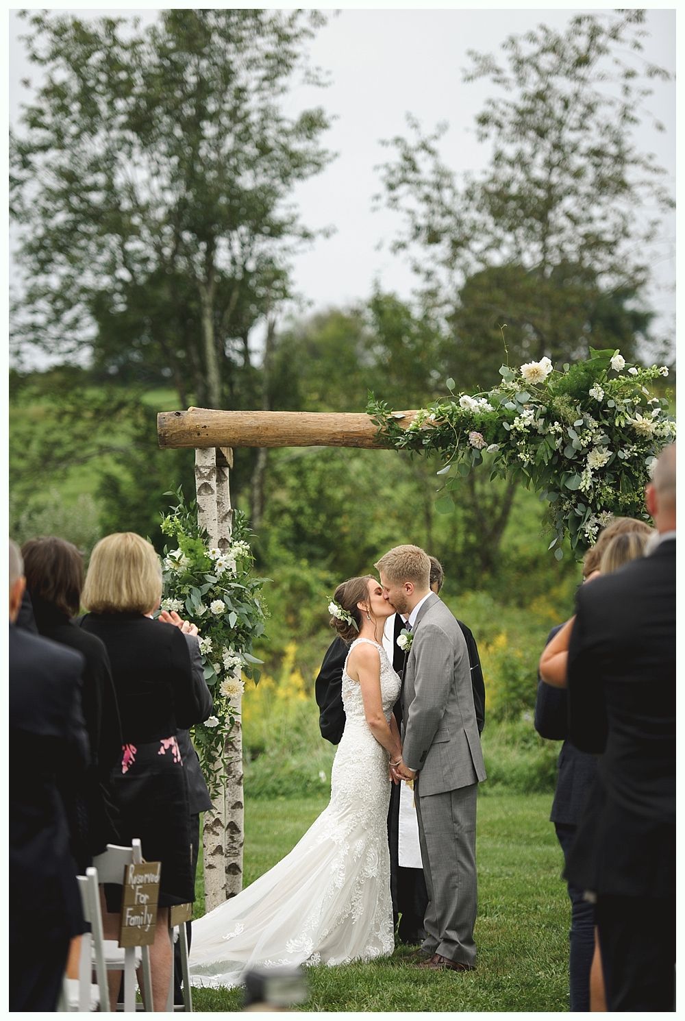 Couple kissing during outdoor wedding ceremony under floral arch.
