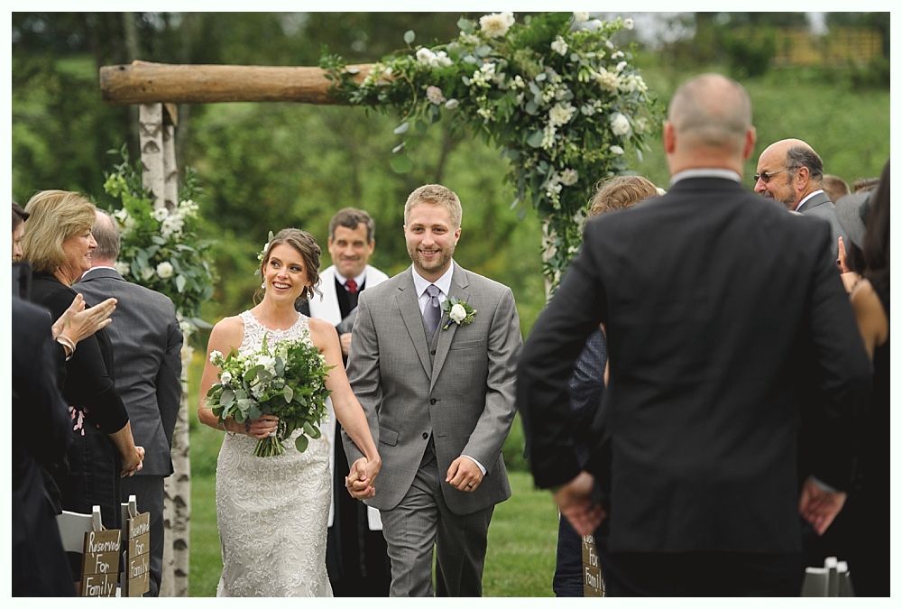 Bride and groom walk happily down aisle after wedding ceremony; floral archway.
