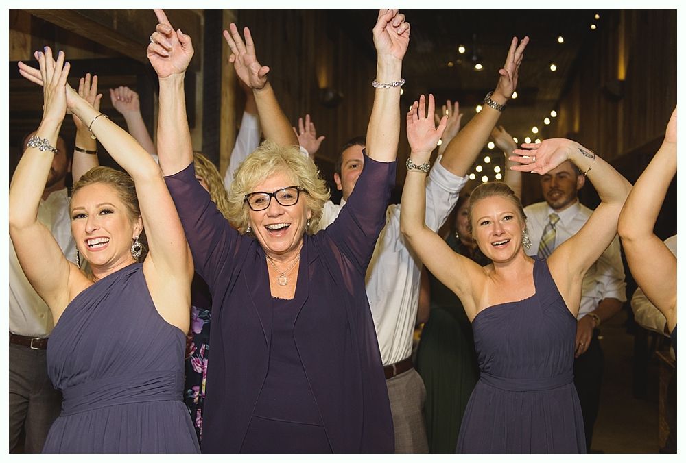 People dancing with arms raised at an event; indoor setting with wooden beams.
