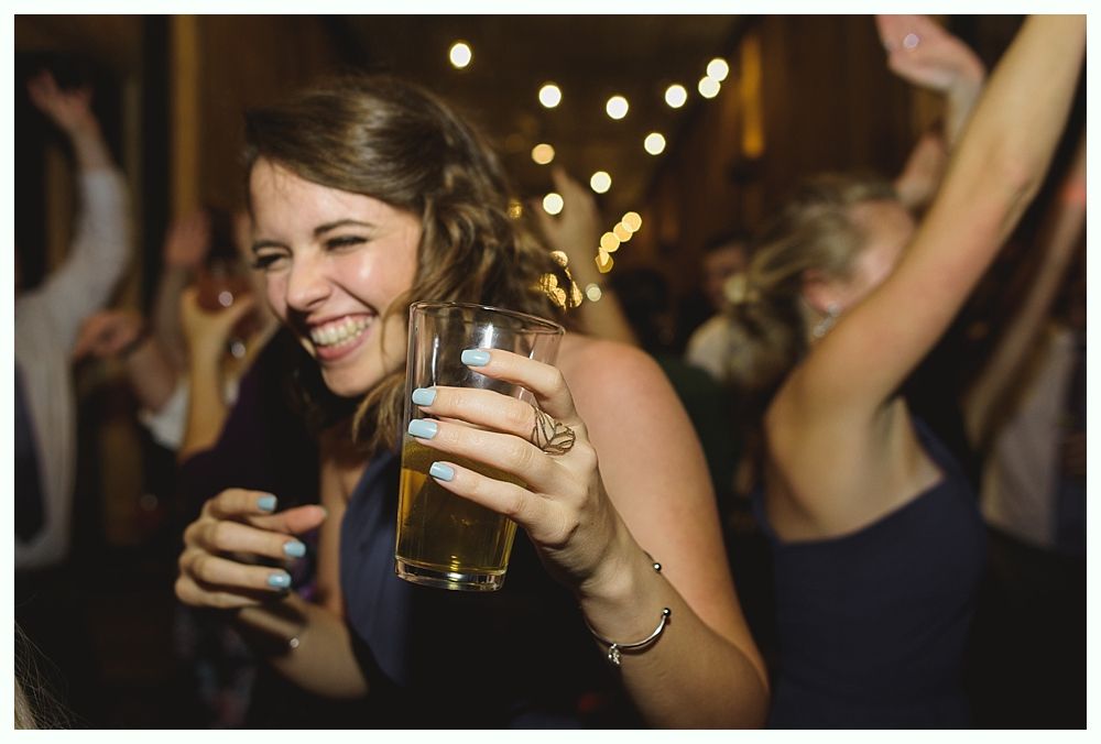 Woman laughing, holding a drink, dancing at a party with others. Warm lighting.