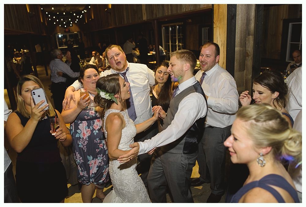 Wedding reception: Bride and groom dancing, surrounded by guests in rustic venue.