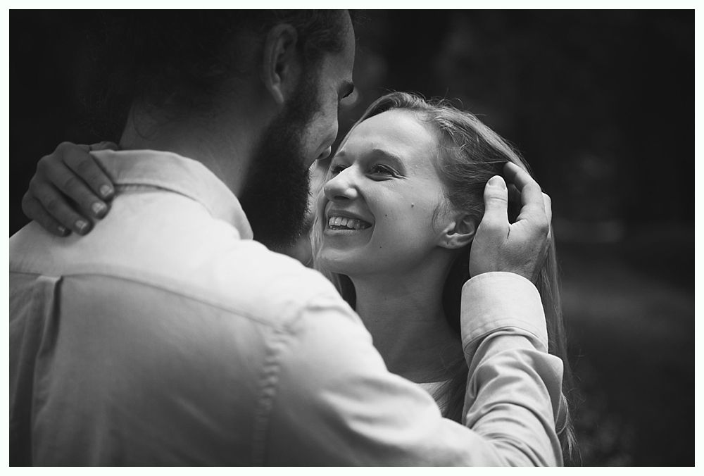 Couple embracing, woman smiling, man's arms around her, soft lighting.