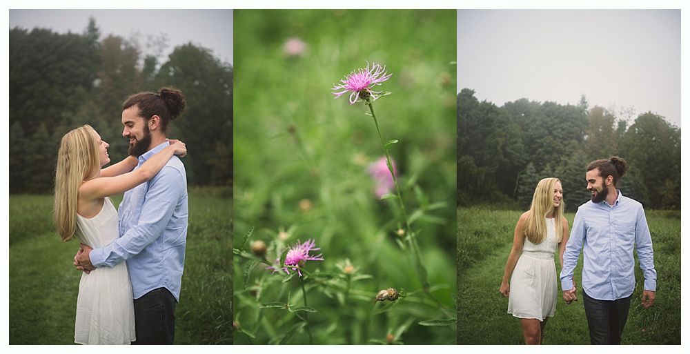 Couple embracing and walking in a grassy field, next to pink wildflowers; trees in the background.