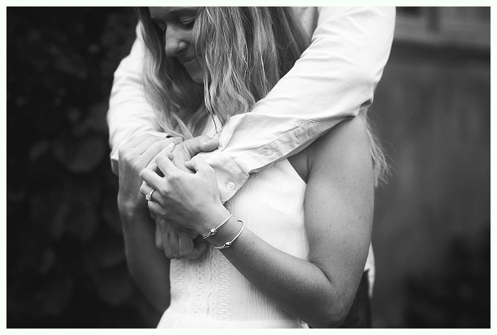 Woman embraced from behind; arms crossed, wearing bracelets.