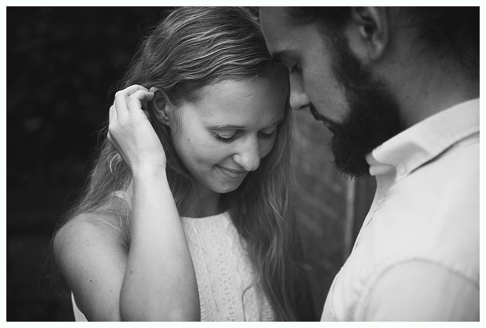 Woman with braided hair smiling, touching her hair, looking down at a man leaning in close, black and white photo.