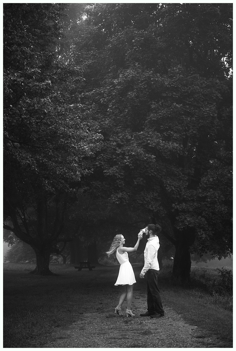 Couple standing beneath large tree, one feeding the other a drink. Black and white.