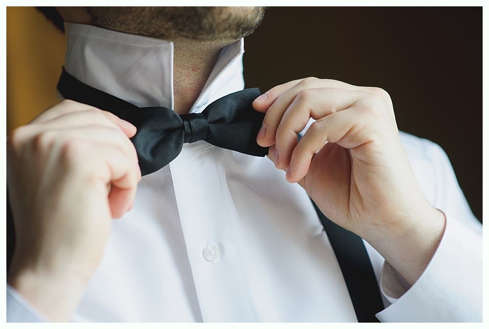 Man adjusting a black bow tie on a white dress shirt.