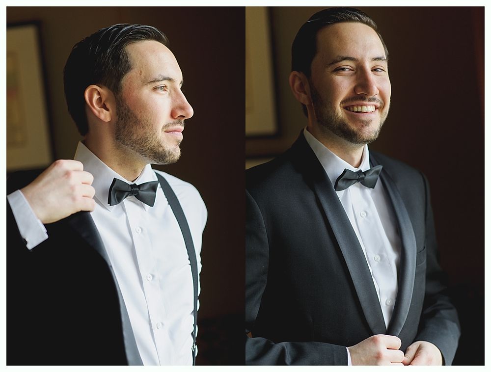 Man in a tuxedo adjusts his bow tie, smiling. Indoors, against a blurred background.